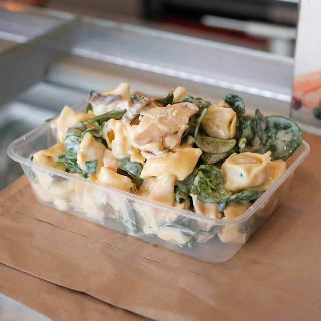 A transparent plastic container filled with a creamy chicken dish.