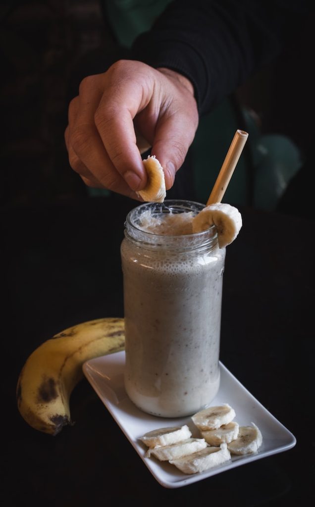 A tall glass filled with banana smoothie with slices of banana for garnish