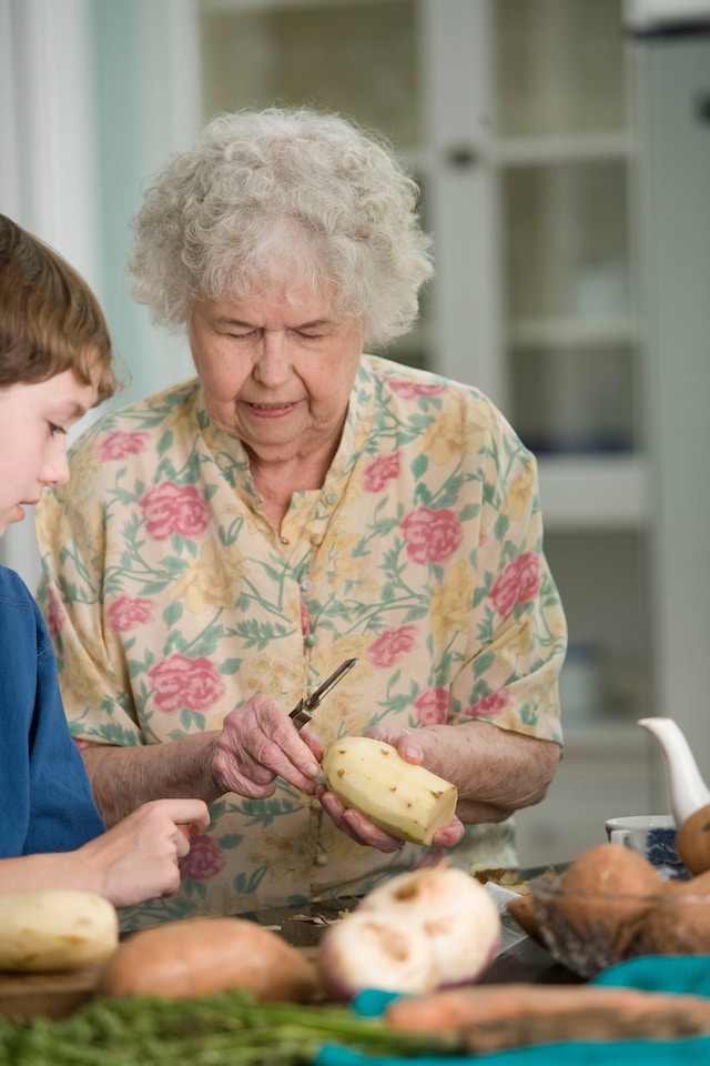Senior woman showing grand child how to peel vegetables