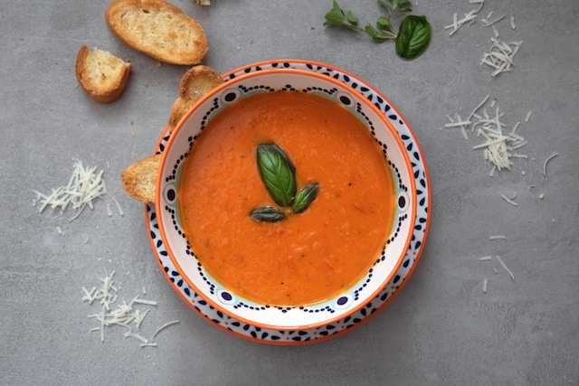 Dark orange soup topped with basil on a ceramic bowl with toasted bread slices on the side