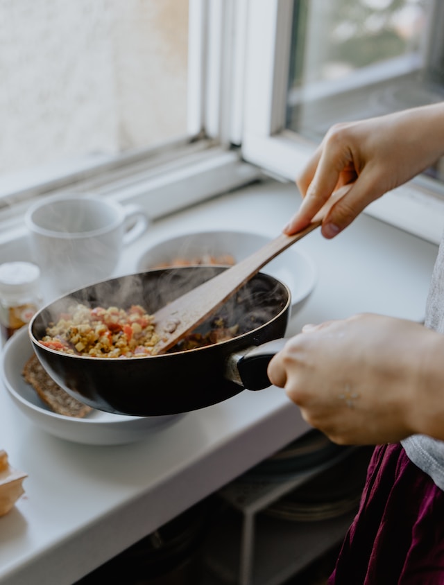 person holding a wooden spatula and frying pan with cooked food
