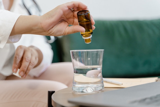Woman pouring essential oil into a glass half-filled with water
