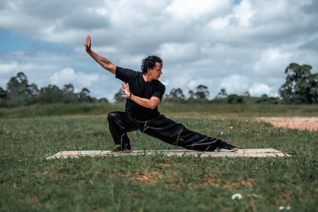 Man in all black performing tai chi in a grassy field