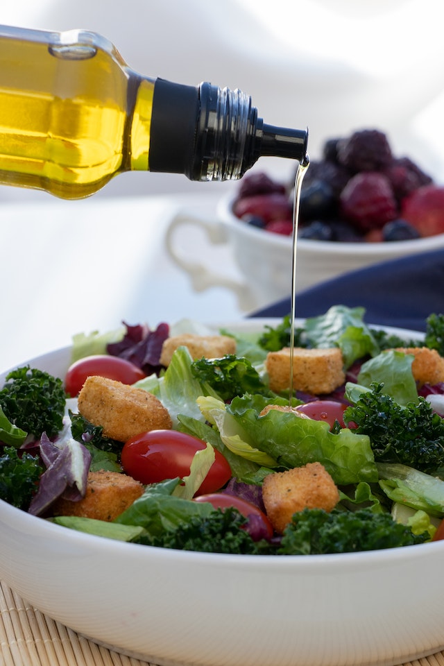 Olive oil being drizzled on a salad in a white ceramic bowl