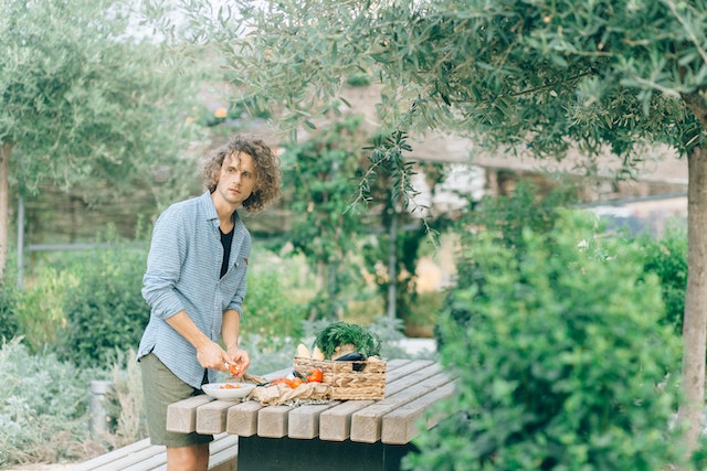 Person slicing vegetables on a wooden table outdoors