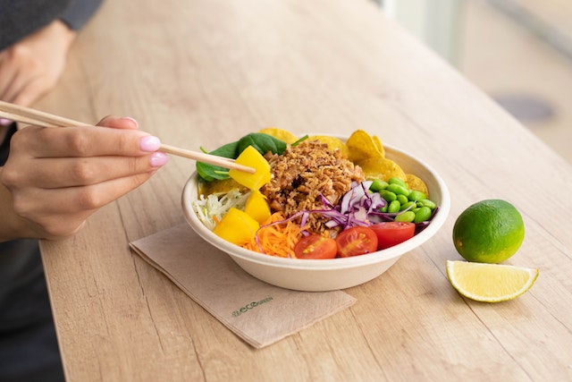 Person holding chopsticks eating a bowl of healthy foods